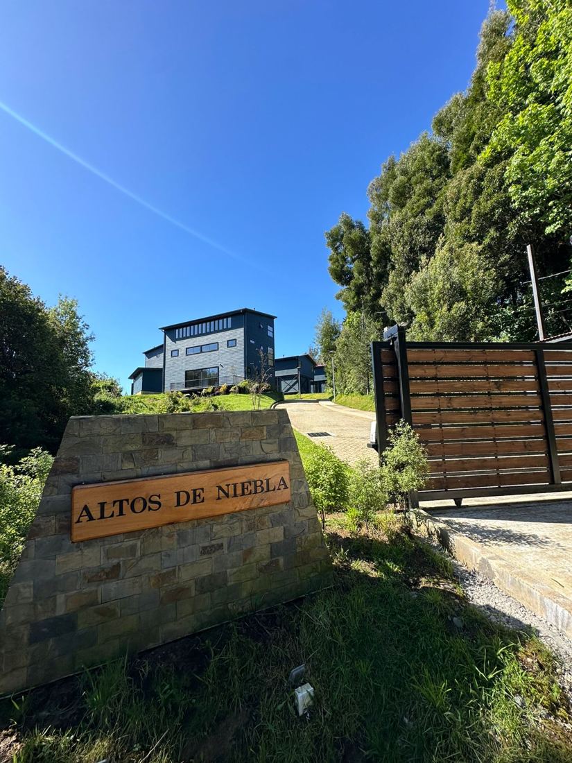 Acceso al condominio Altos de Niebla con su letrero de piedra y madera
